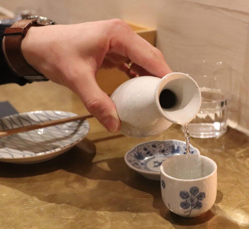 the hand of guy while he is pouring sake at the Japanese restaurant in East London
