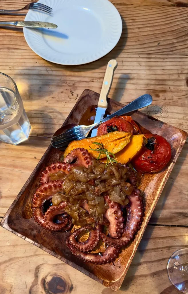 Whole octopus served on a wooden tray with roasted tomatoes and potatoes at Cantina 32 a restaurant in Porto