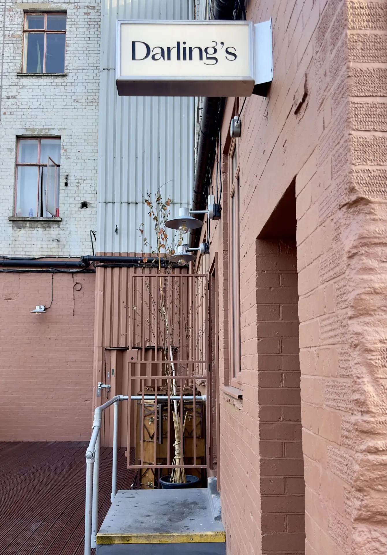 A brick building exterior with a sign reading "Darling's" above a door. A small patio area with potted plants is visible next to the entrance.