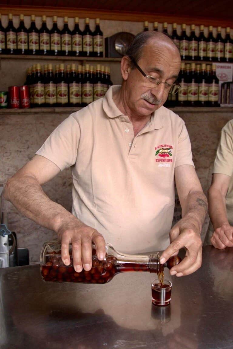 A man elegantly pours Ginjinha, a Portuguese liqueur from the bottle, capturing the essence of Lisbon's vibrant culture and culinary tradition