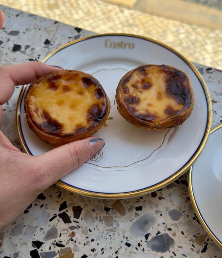 A person displays a plate with two small, delicious Pastel de Nata pies, showcasing their golden crust and creamy filling.