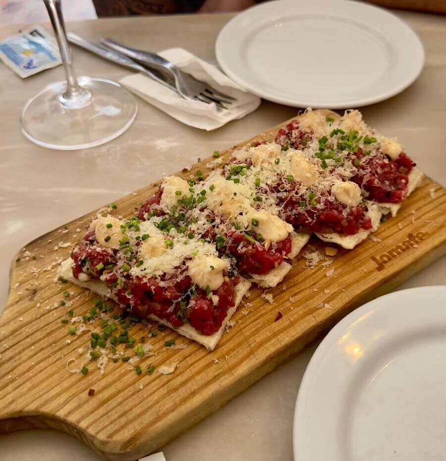A wooden cutting board displaying veal tartare, representing a culinary highlight from Lisbon's Taberna Da Rua Das Flores.