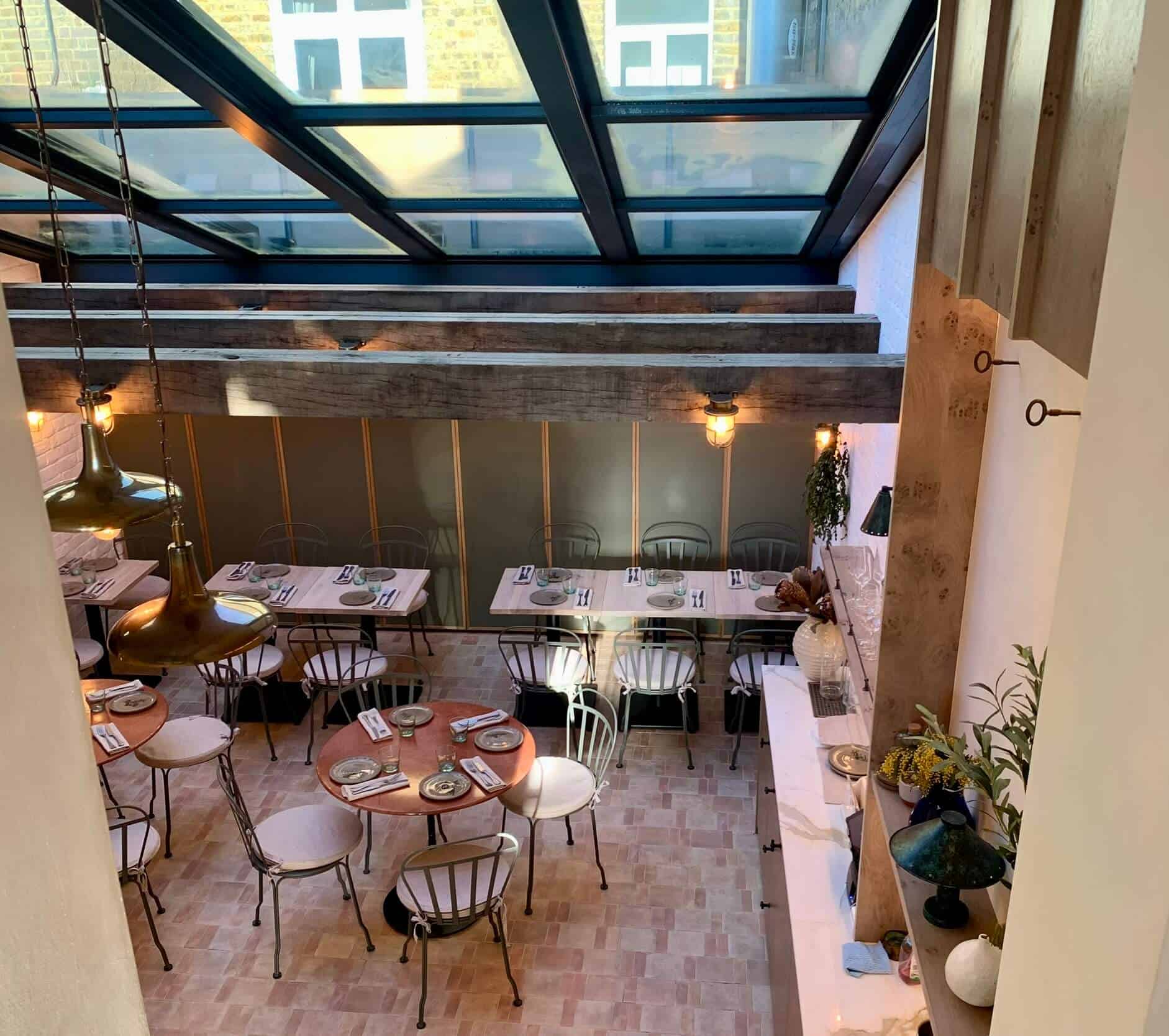 Interior design of a restaurant that has earthy colours like blush, green, brown. A skylight roof allow the daylight to come through.