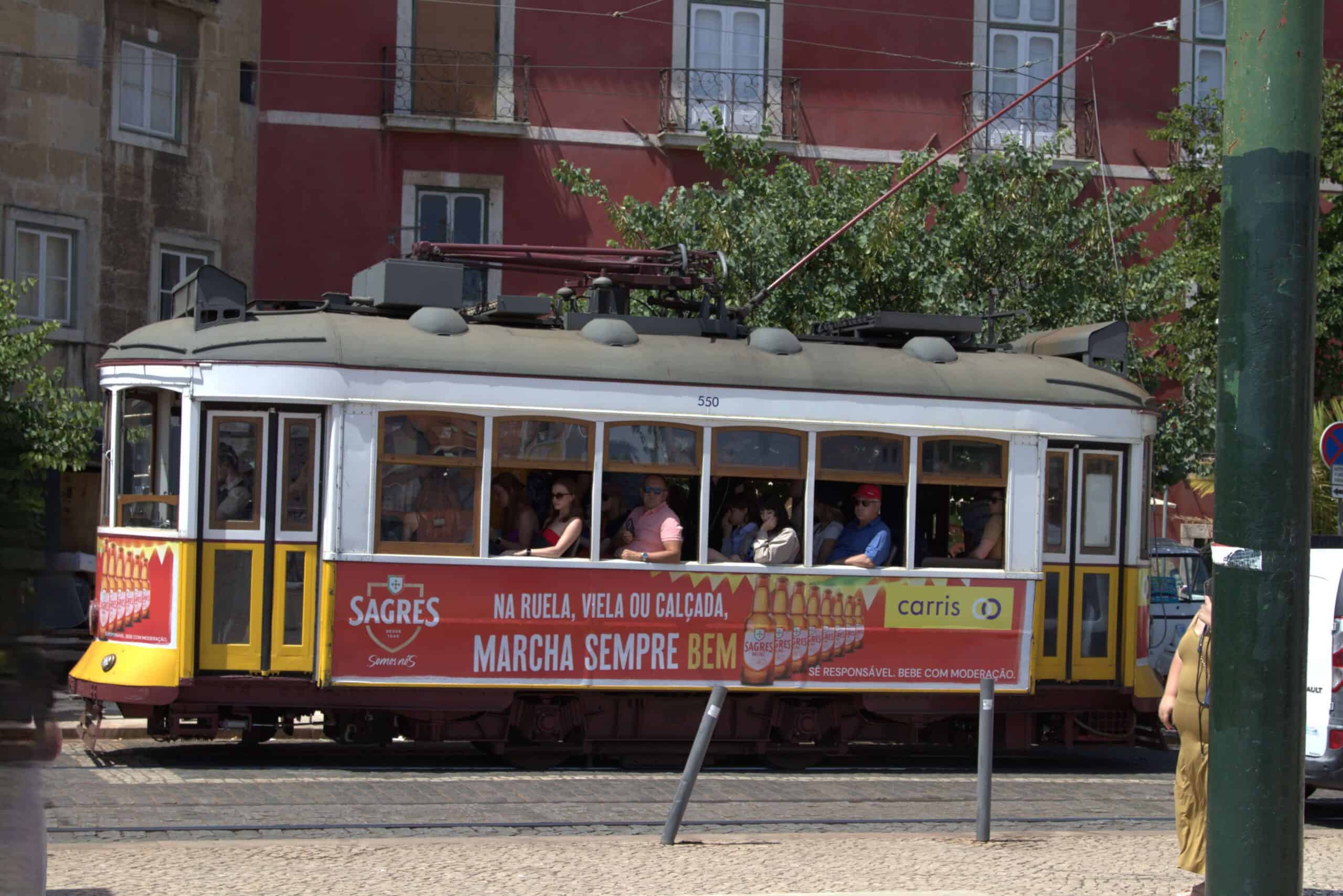 A traditional yellow tram in Lisbon filled with tourists looking out the street view