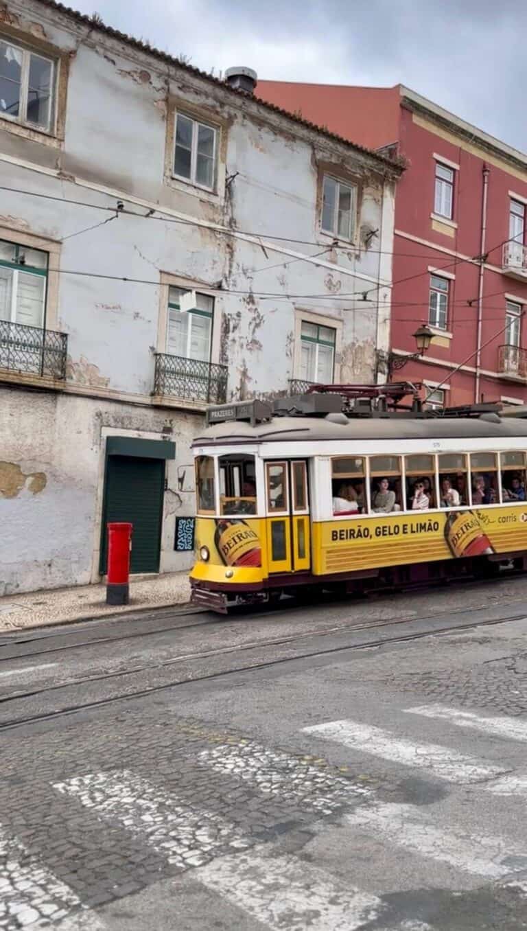 Traditional yellow tram 28 passing on Lisbon cobblestone street