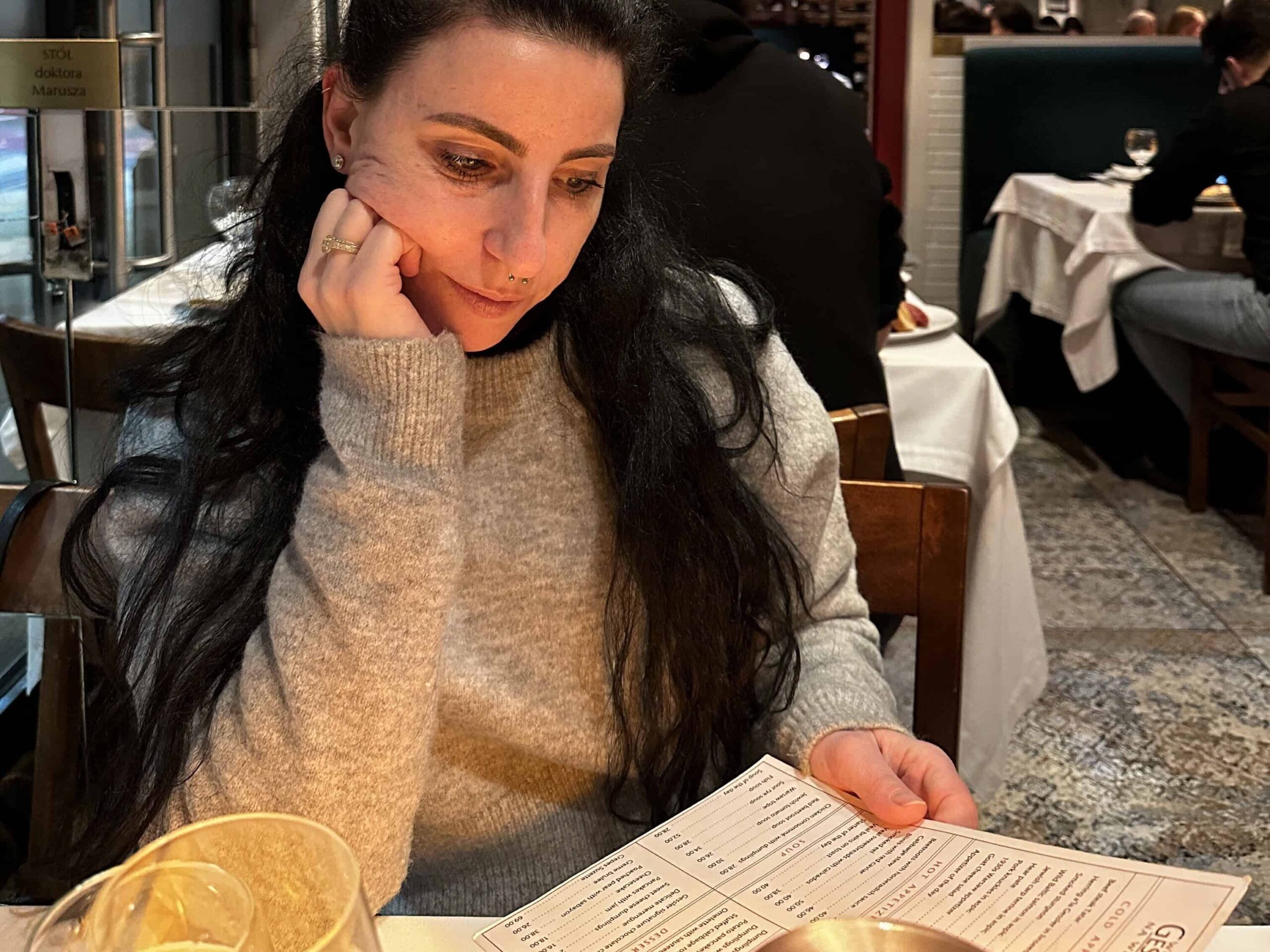 Sara, owner of Exploring the Food Scene, a London Food Travel Blogger while reading a menu in a cosy, stylish restaurant in Warsaw.