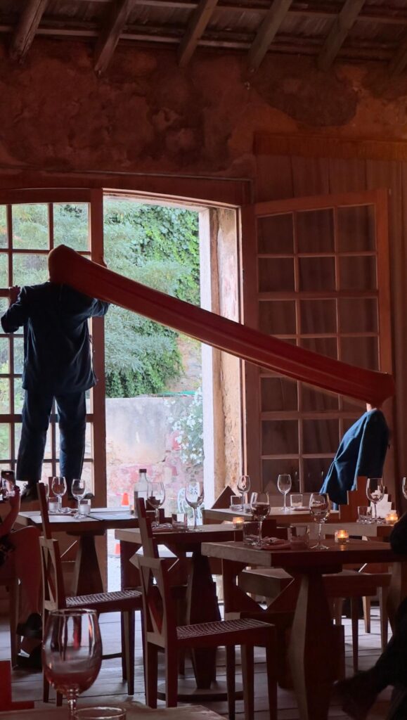 Two performers in blue suits connected by a long orange tube during a live art show at Palacio do Grilo restaurant in Lisbon