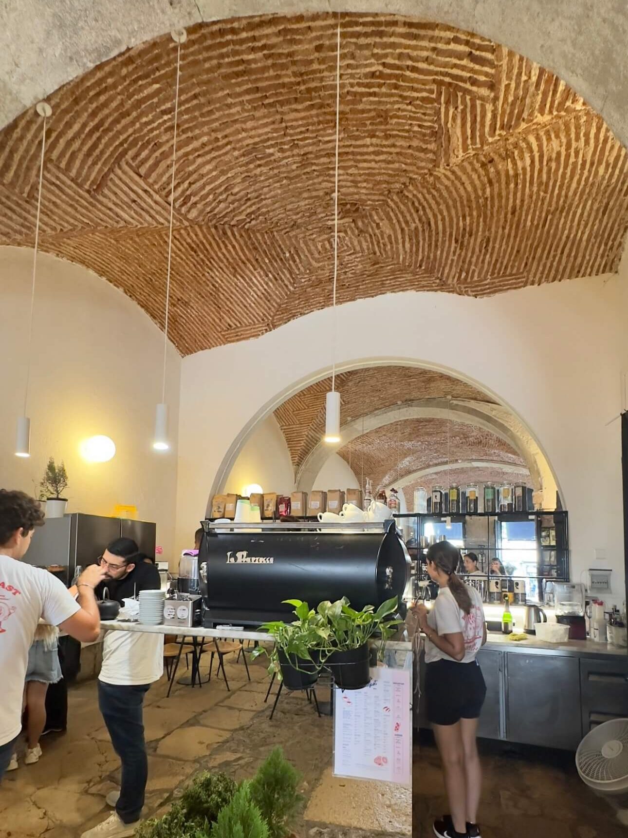 The interior of Dear Breakfast in Alfama, featuring a beautiful historic brick arched ceiling, stone floors, and a busy coffee counter