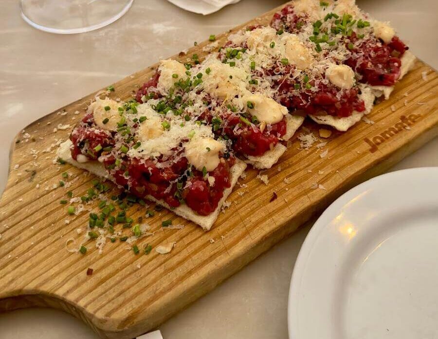 A wooden cutting board displaying veal tartare, representing a culinary highlight from Lisbon's Taberna Da Rua Das Flores.