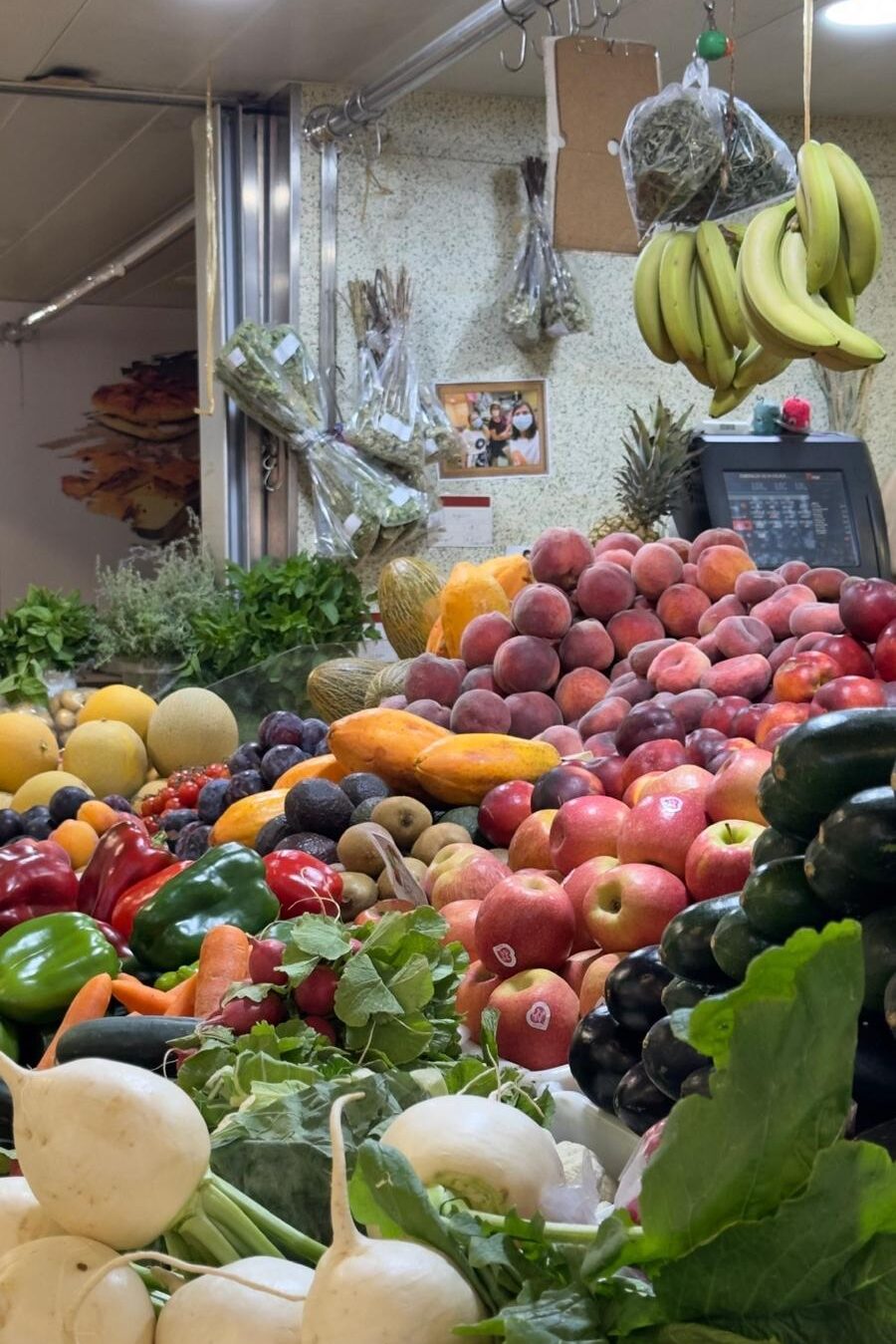 A vibrant, overflowing display of fresh local fruits and vegetables at the Mercado Municipal de Faro, showcasing piles of apples, peaches, peppers, and hanging bananas.