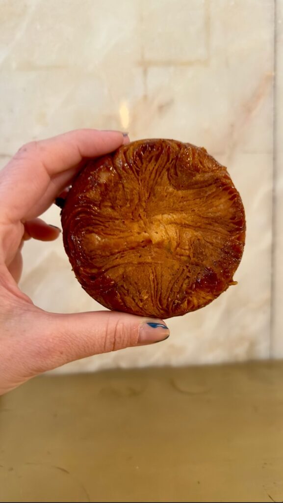 My hand holding a perfectly caramelized, golden-brown Kouign-Amann pastry at Lully bakery, featured in a guide to the best bakeries in Lisbon.