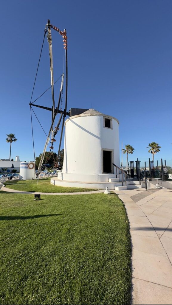 The exterior of the historic 1938 white windmill housing the Windmill restaurant in Albufeira, featuring its large traditional sails against a bright blue sky.