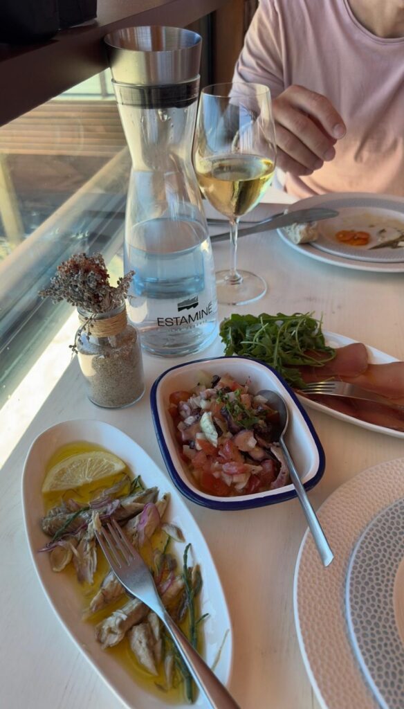 A dining table at Estaminé restaurant featuring a bottle of desalinated water, a glass of white wine, and traditional starters including marinated cavalinhas fish and octopus salad.