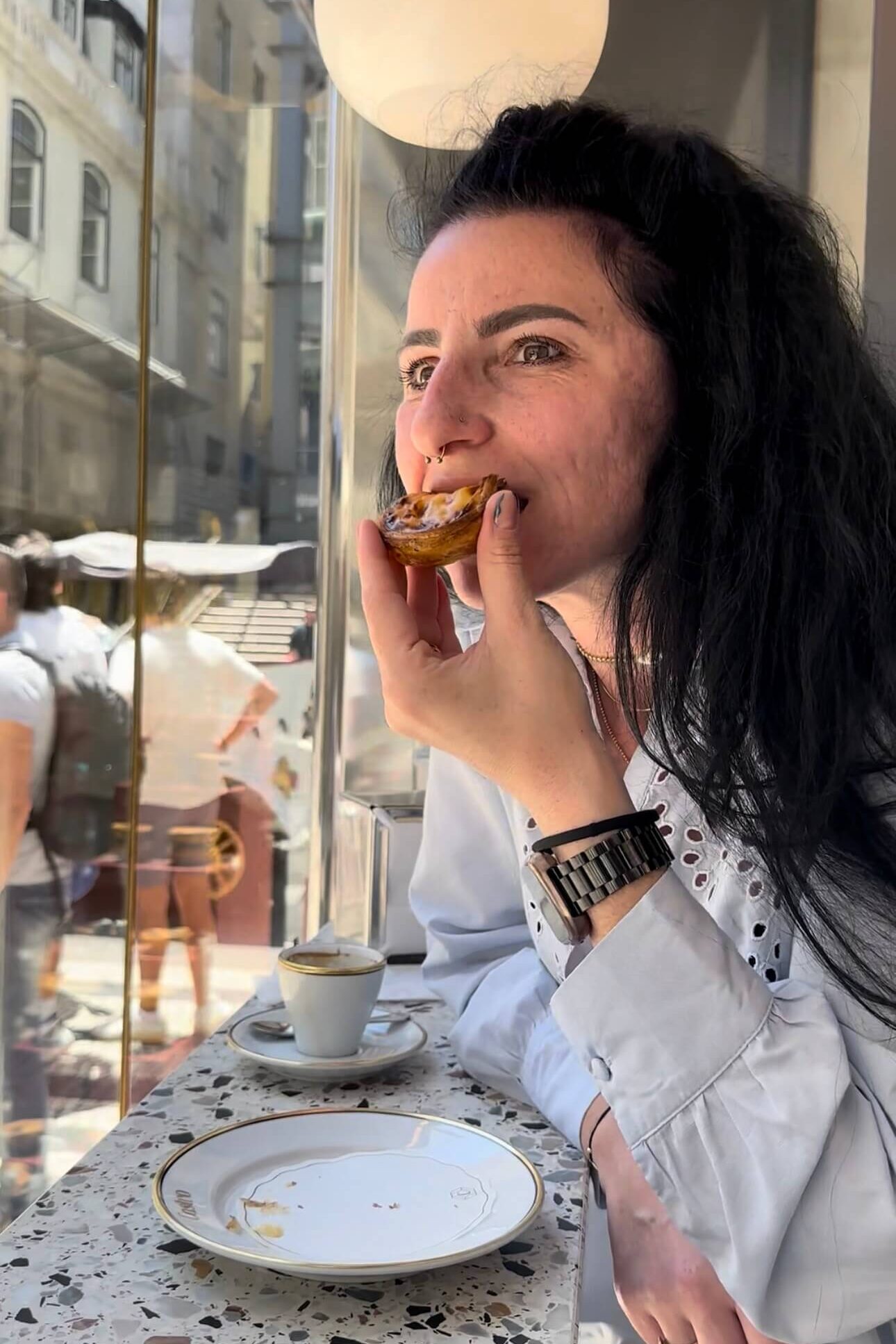 Blog author Sara sitting by the window inside Castro boutique shop, eating a traditional pastel de nata with an espresso cup on the counter, featured in her Lisbon food guide