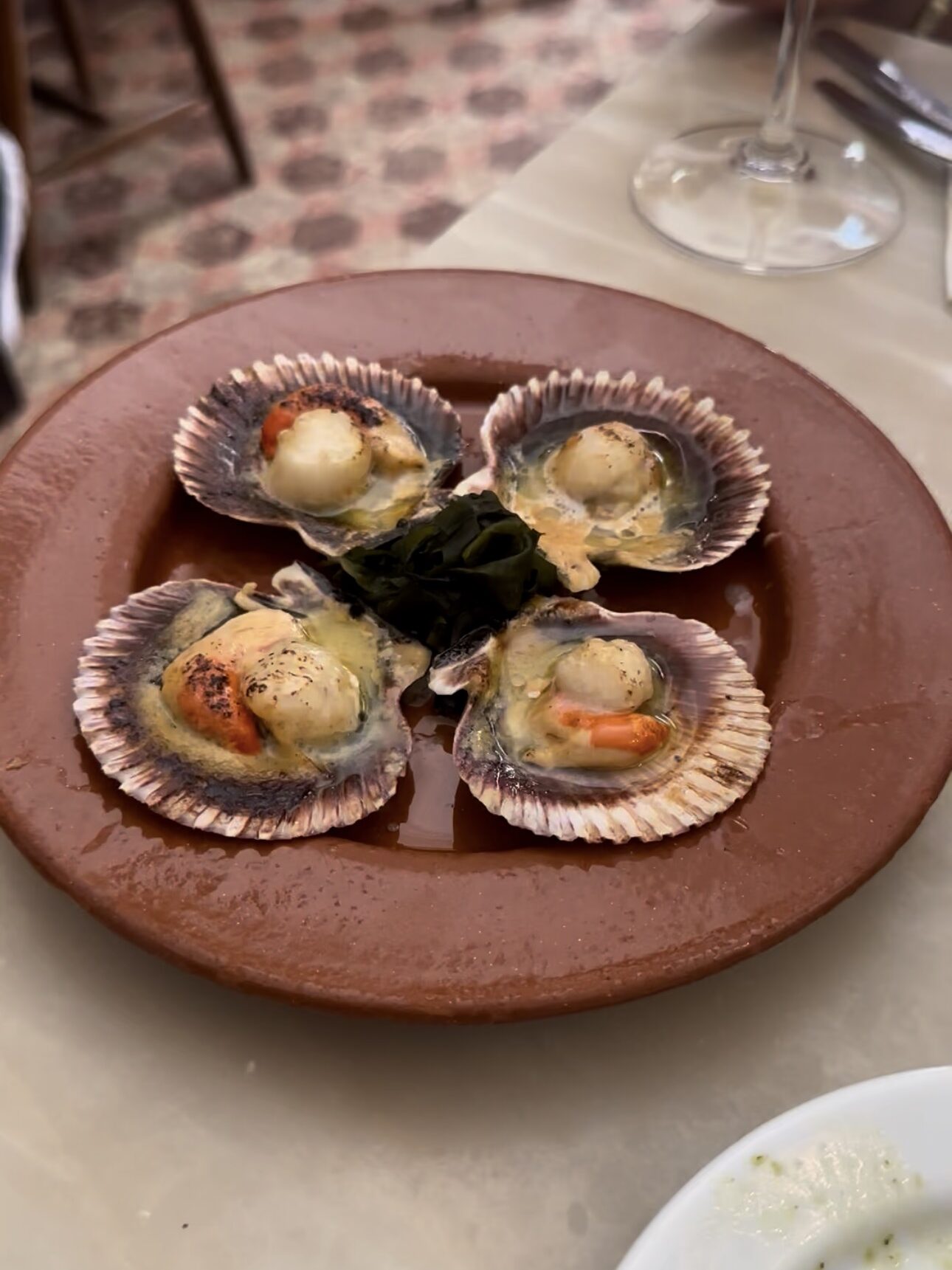 Four smoked scallops served in their shells on a rustic clay plate at Taberna Da Rua Das Flores, one of the best restaurants in Lisbon.