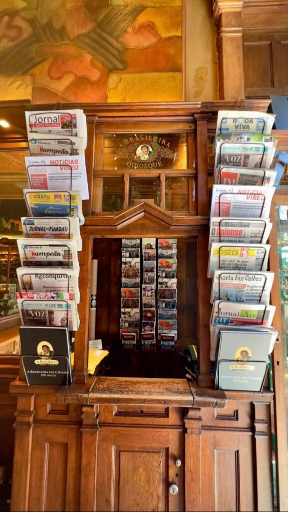 An old-fashioned wooden newspaper stand and kiosk filled with local papers and postcards inside A Brasileira, one of the most famous historic cafes in Lisbon.