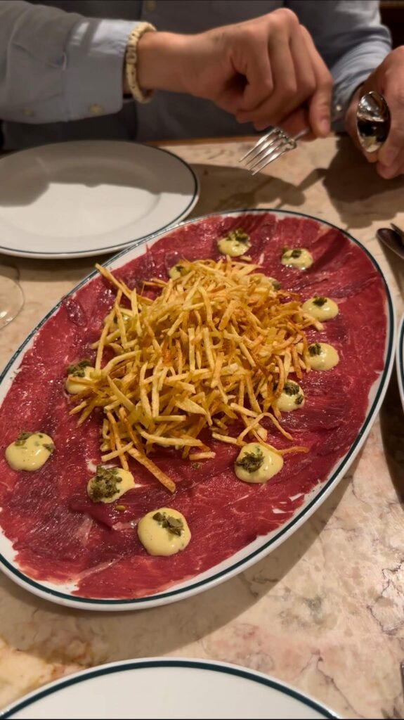 An oval platter of thinly sliced Arouquesa beef carpaccio dressed with dots of capers vinaigrette and a mountain of crisp shoestring fries at Canalha, highlighted in a Lisbon food guide