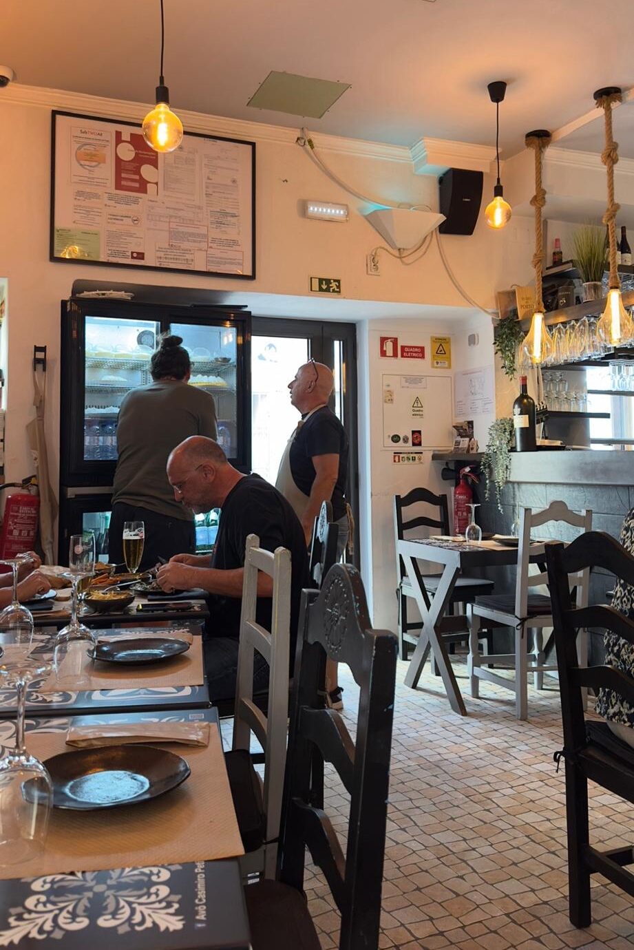 The cozy, traditional interior of Avô Casimiro restaurant in Portimão, showing patrons dining at tables under warm glowing light bulbs in an authentic Portuguese tasca.