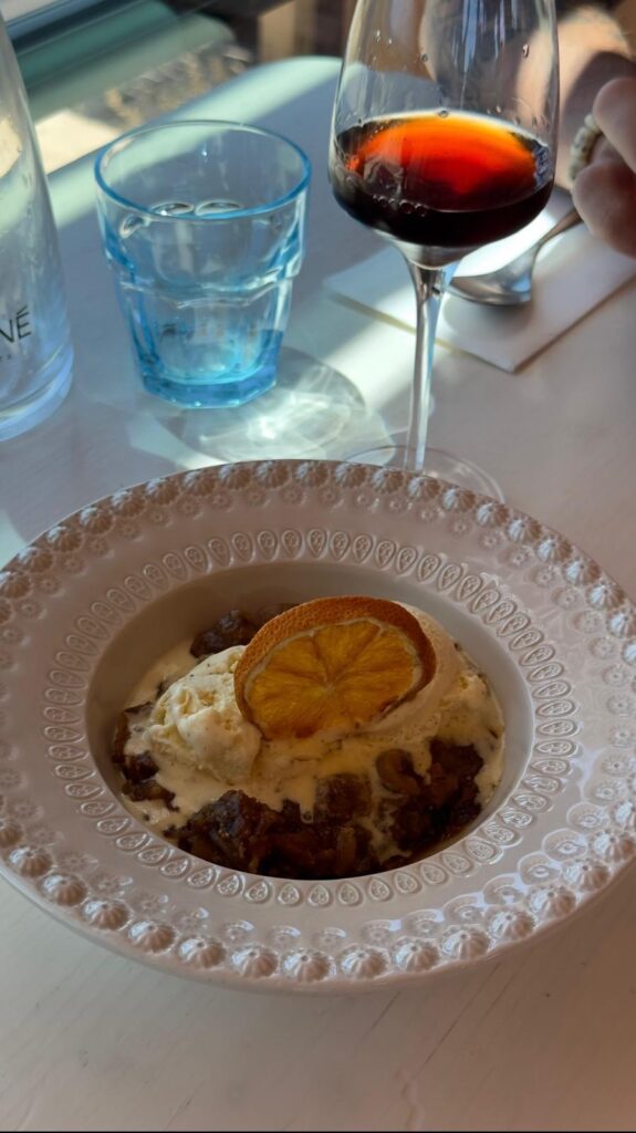 A beautifully plated dessert bowl at Estaminé containing rich sweets topped with scoops of vanilla ice cream and a dehydrated orange slice, next to a glass of fortified dessert wine.