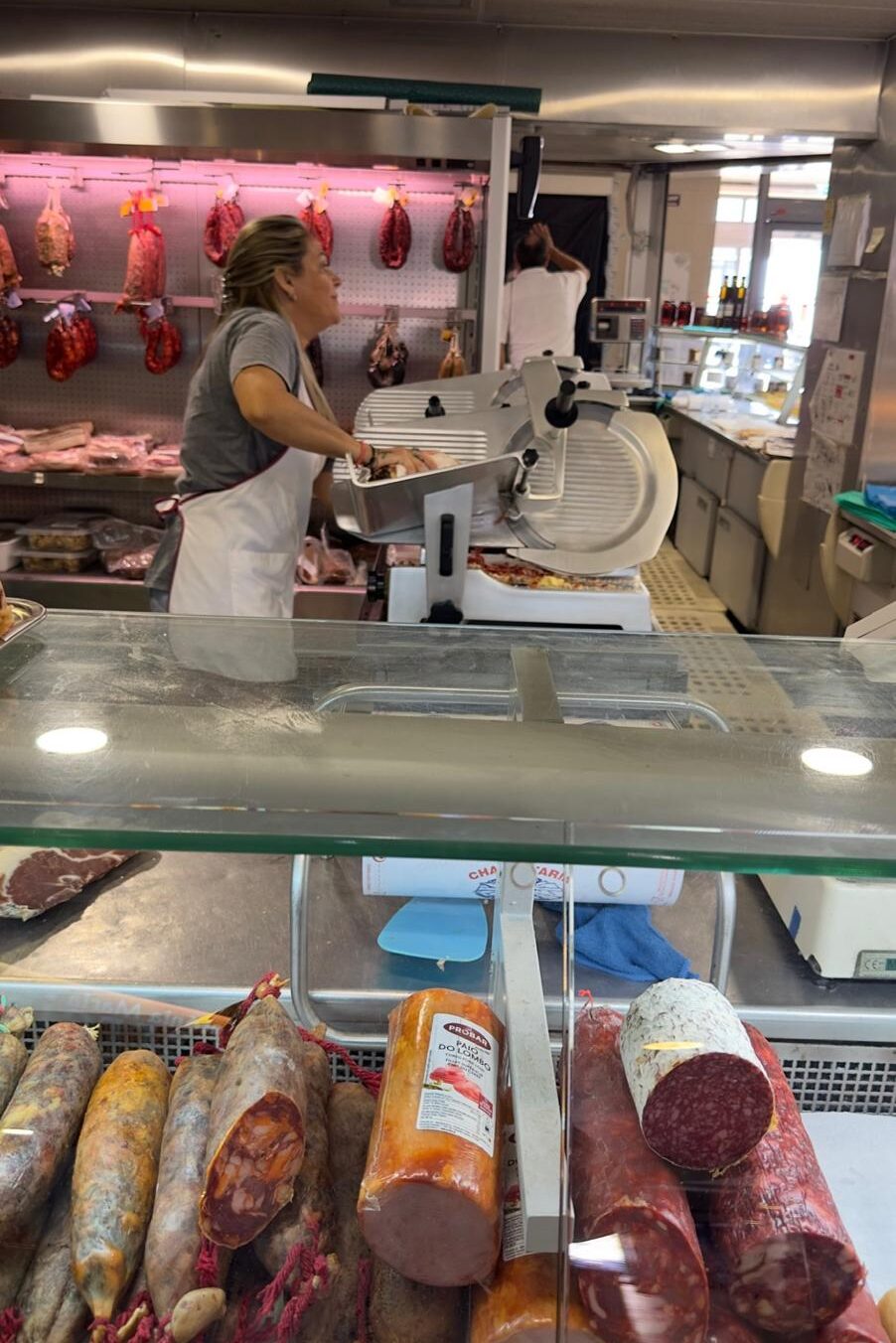 A vendor slicing local cured meats behind a glass deli counter displaying traditional Portuguese sausages and chouriço at the Mercado Municipal de Faro.