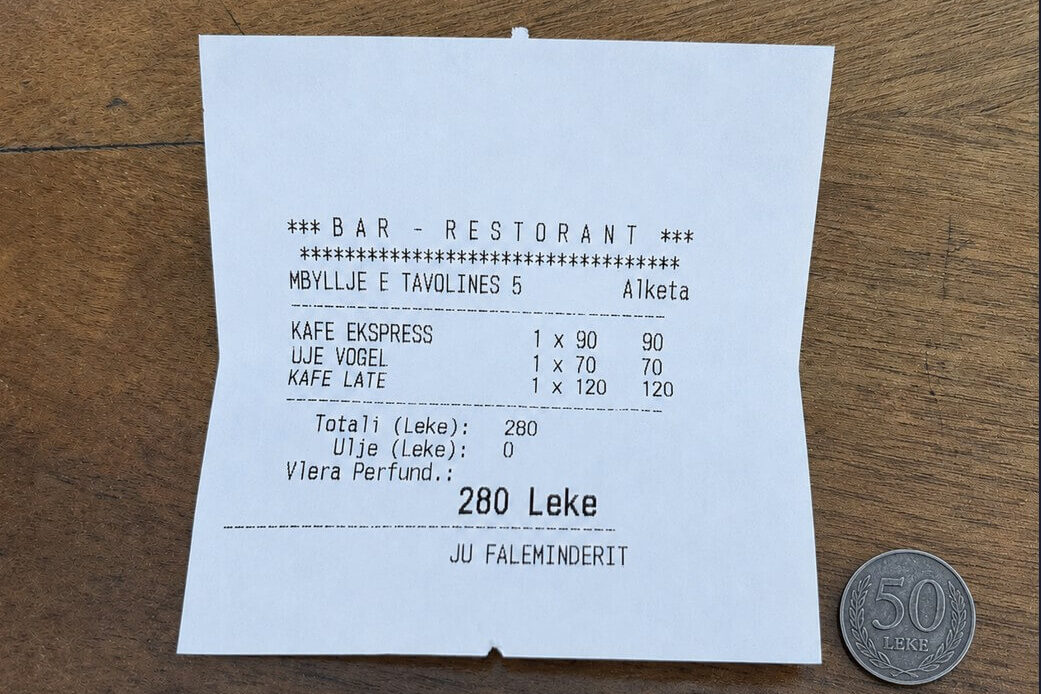 Albanian cafe bill with a 50 lek coin left as a tip